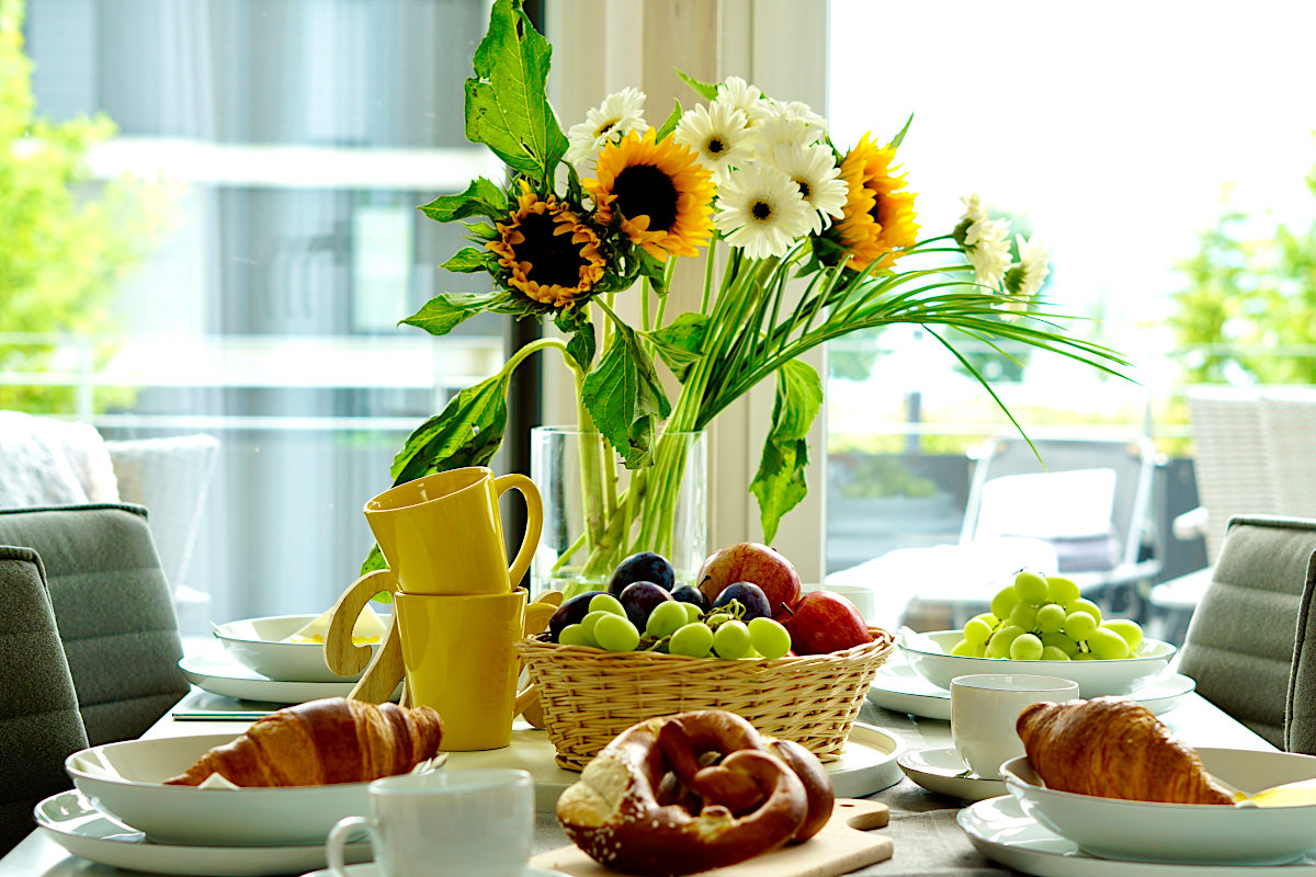 gedeckter-tisch-mit-crossaint-trauben-aepfel-brezel-sonnenblumen