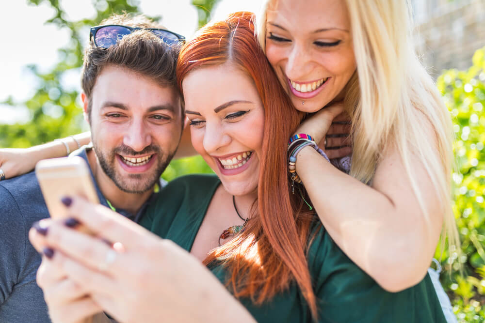 Roaming am Bodensee vermeiden – So schützen Sie Ihren Geldbeutel und Ihr Handy 1 Drei junge Personen blicken gemeinsam auf ein Smartphone – ein typischer Urlaubs-Moment mit Selfie oder Anruf, doch die Roaming-Gefahr lauert.