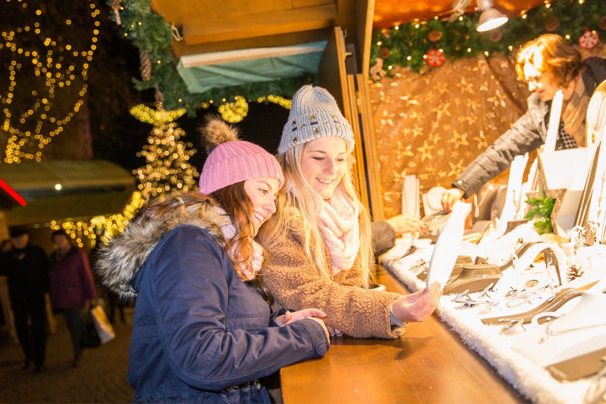 Weihnachtsmarkt am Bodensee 2025: Diese 8 Märkte lohnen sich 1 Zwei Frauen schauen sich handwerkliche Holzarbeiten an einem Stand auf dem Weihnachtsmarkt in Friedrichshafen an