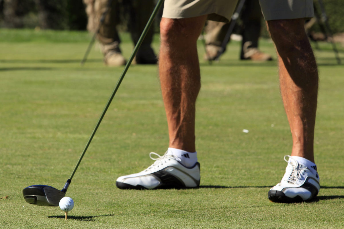 Golfer beim Abschlag auf grünem Golfplatz mit viel Grün und hellem Licht